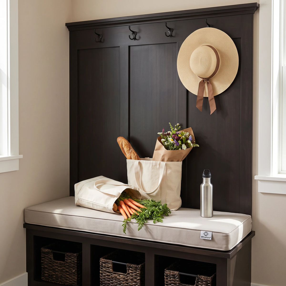 Dark wood entryway bench with a cushioned seat, built-in storage baskets, coat hooks, and a wall-mounted hat rack. A cream tote bag, bread bag, flowers, carrots, and a silver water bottle sit on the bench, with a straw hat hanging on the wall. - view 4