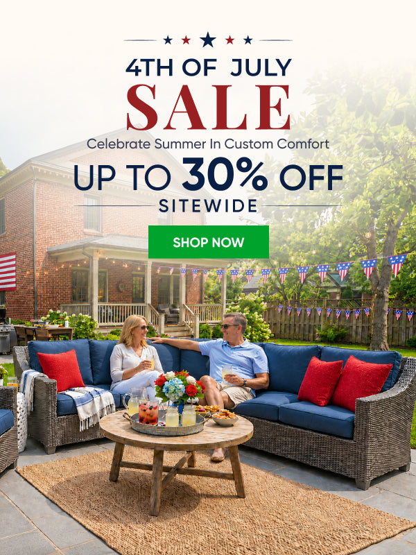 Couple relaxing on navy cushioned wicker sofas with red pillows on patio; 4th of July sale, up to 30% off sitewide.